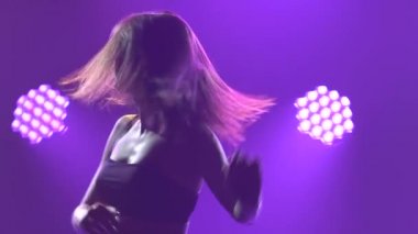 Esnek kadın dansçı döner ve zıplar. Karanlık bir stüdyoda mor ışıklarla dans eder. İnce bir vücudun silueti. Yaklaş. Yavaş çekim.