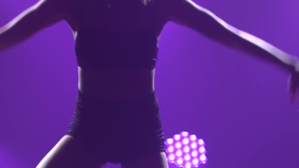 这个性感的女舞蹈演员旋转着跳跃着，带着紫色的灯光在黑暗的工作室里跳着蔑视的舞。细长身体的轮廓非常接近。慢动作. — 图库视频影像