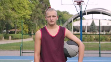 Açık havada basketbol oynadıktan sonra top oynayan neşeli bir gencin portresi. Caddede kameraya gülümseyen neşeli erkek sokak basketbolcusu. Kapatın. Yavaş çekim.