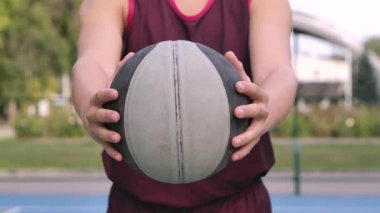 Basketbolcu bir adam topu elinde tutuyor ve kameraya doğru tutuyor. Yazın açık hava eğitimi. Sağlıklı ve aktif bir yaşam tarzı. Top ve erkek gövdesi çok yakın. Yavaş çekim.