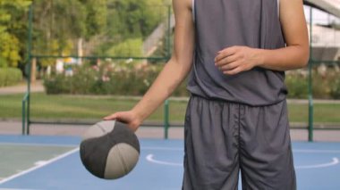 Basketbolcu adam oyun alanında bacaklarının arasına top sürüyor. Yaz maçının tadını çıkar. Top ve erkek gövdesi çok yakın. Yavaş çekim.