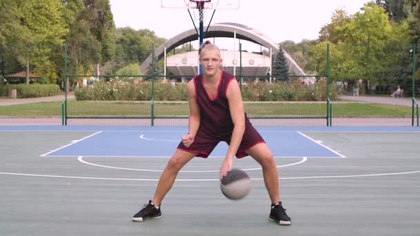Aktiva manliga basketspelare öva bollhantering färdigheter genom att dribbla bollen mellan benen utomhus. Närbild. Långsamma rörelser. — Stockvideo
