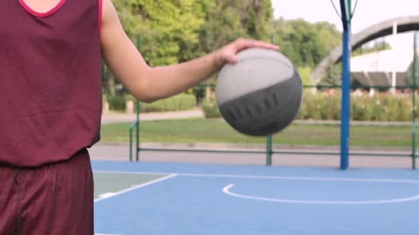 Nastolatek bawi się koszykówką na placu zabaw. Facet uderza piłką w podłogę. Piłka i chłopaki tułów blisko. Zwolniony ruch. — Wideo stockowe