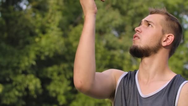 Vue latérale du jeune joueur de basket-ball se tient sur le terrain extérieur et la balle filante sur le doigt. Homme en tenue de sport se reposant après un match de streetball dans la rue. Ferme là. Mouvement lent. — Video