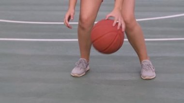 Genç bir kız basketbolcunun yerel sahada antrenman ve egzersiz görüntüleri. Topla salyalarını akıtıyor. Bacaklar spor ayakkabılarda, yakın çekim. Yavaş çekim.