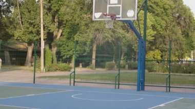 Basketbol potasında başarılı bir gol atma girişimi. Genç adam şehir merkezindeki parkın yakınındaki özel bir alanda oynuyor. Sporcu sokak basketbolu antrenmanı yapıyor. Kapatın. Yavaş çekim.