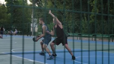 Spor sahasının arkasında, yazın açık havada basketbol oynayan iki adamın görüntüsü. Sportif yaşam tarzı. Kapatın. Yavaş çekim.