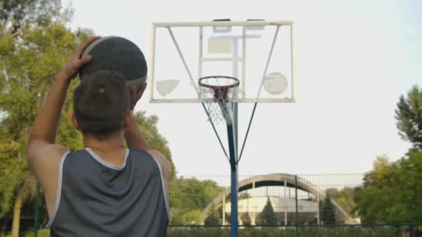 Vista posterior de un jugador irreconocible lanzando una pelota en un aro de baloncesto, la pelota golpea el ring y anota. De cerca. Movimiento lento. — Vídeo de stock