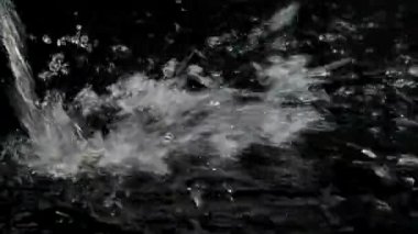 Dalgalı su yavaşça karanlık yüzeye düşüyor ve sıçrıyor. İnanılmaz bir atıştı. Mükemmel giriş için siyah zemin üzerinde güzel bir su oyunu.