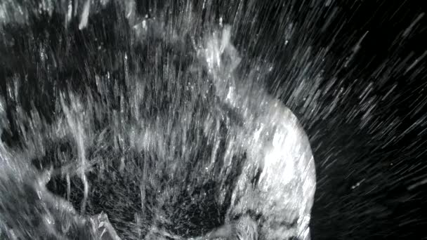 Objekt padající do vody shora a stříkající kapky tekutiny na černé pozadí. Krásné texturované pozadí s lesklými cákanci vody ve zpomaleném filmu zblízka. — Stock video