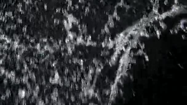 Spraya vatten spricker från botten på svart bakgrund. Vattenstänk från ett föremål som träffar vattenytan. Vacker strukturerad bakgrund med blanka stänk av vatten i slow motion närbild. — Stockvideo