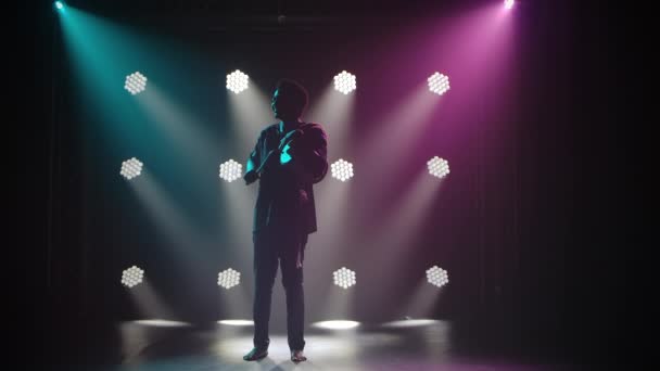 Silhouette of Musiker spielt die afrikanische sprechende Trommel Yuka in einem dunklen Studio vor dem Hintergrund der Lichter. Der schwarze Mann genießt die Musik und lächelt. Afrikanische Folklore. Zeitlupe. — Stockvideo