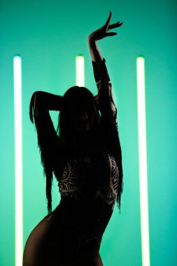 Elleri havada zarif poz veren çekici bir kadın silueti. Stüdyoda bir kadın neon lambaların arkasında duruyor..