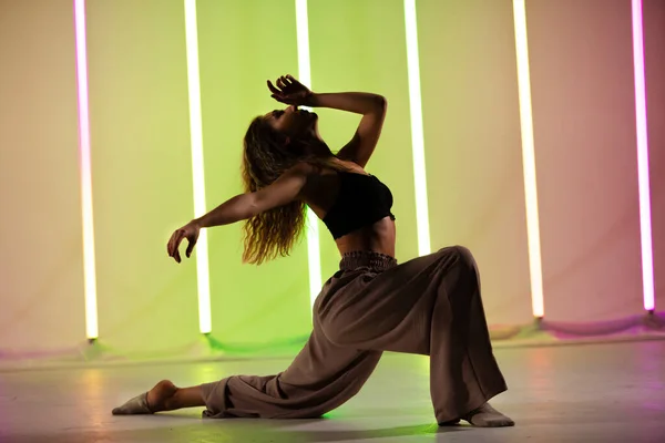 Retrato de uma bela dançarina moderna em uma bela pose de dança contra o pano de fundo de lâmpadas de néon com luz colorida. — Fotografia de Stock