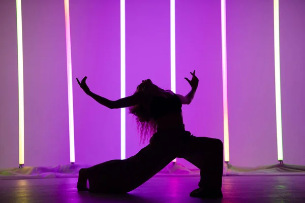 在霓虹灯的映衬下，一位当代女舞蹈演员在演播室里表演的轮廓。跳舞的女人摆出一副与世隔绝的姿势. — 图库照片