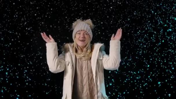 Portret van een gelukkige jonge vrouw die geniet van de eerste sneeuw en een duimgebaar maakt. Blond op een zwarte achtergrond tussen vallende sneeuwvlokken. Nieuwjaar. Kerstvakantie. Langzame beweging. Sluiten.. — Stockvideo