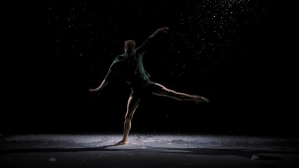 Hedendaags ballet, een man voert elementen van de moderne choreografie en springt in de schijnwerpers. Silhouet van een danser tegen de achtergrond van vallende sneeuw. Langzame beweging. — Stockvideo