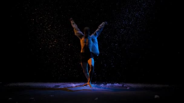 Emotionele uitvoering van hedendaagse choreografie of modern ballet. Een silhouet van een man tegen de achtergrond van vallende sneeuw in de stralen van studio licht. Winters verhaal. Langzame beweging. — Stockvideo