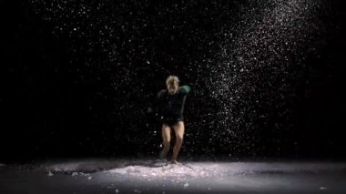 Adam modern balenin dramatik danslarını yapıyor. Bale dansçısı, kar ve stüdyo ışıklarının arka planına karşı modern koreografi sergileyerek plastikle hareket eder. Yavaş çekim.