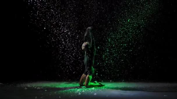 De mens danst de dramatische dansen van het moderne ballet. Ballet danser beweegt met plastic, het uitvoeren van moderne choreografie tegen de achtergrond van vallende sneeuw en veelkleurige studio licht. Langzame beweging. — Stockvideo