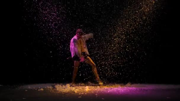 De mens danst de dramatische dansen van het moderne ballet. Ballet danser beweegt met plastic, het uitvoeren van moderne choreografie tegen de achtergrond van vallende sneeuw en veelkleurige studio licht. Langzame beweging. — Stockvideo