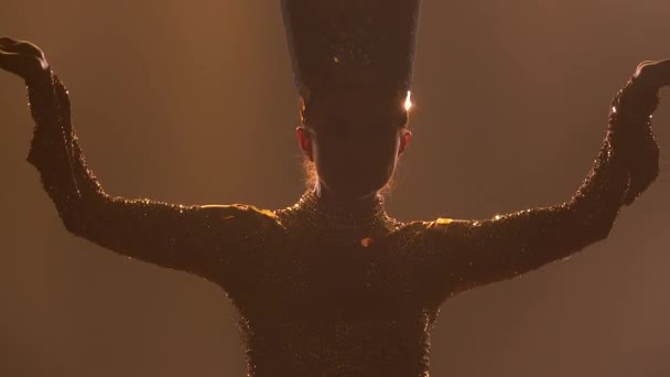 Spectacle théâtral de danse. Actrice, habillée comme la reine de l'Egypte ancienne, danse dans un studio sombre. Silhouette de femmes fines sur un fond fumé avec rétro-éclairage. Gros plan. — Video