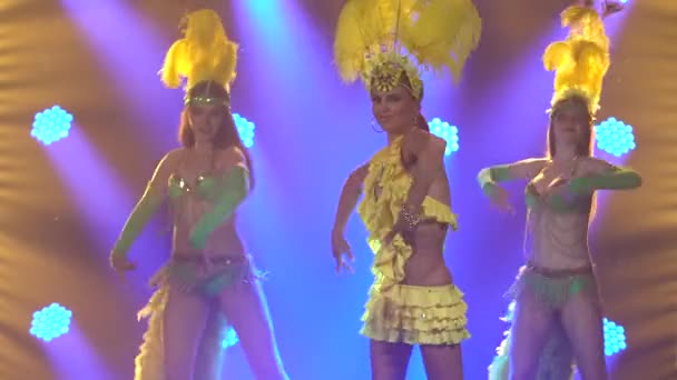 Schöne lächelnde junge Frauen tanzen Samba in traditionellen brasilianischen Karnevalskostümen. Gedreht in einem dunklen Studio mit blauem Neonlicht im Hintergrund. Nahaufnahme. — Stockvideo