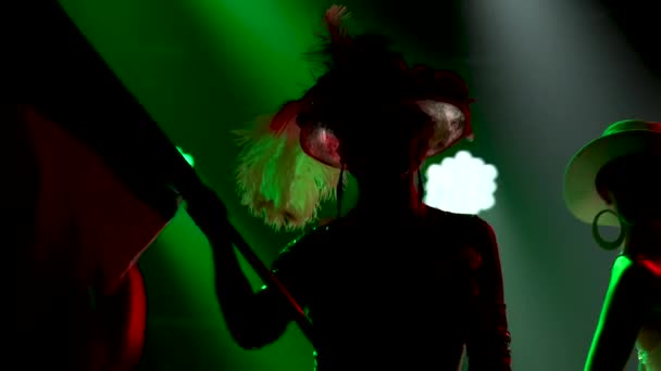 Silhouettes of three glamorous ladies are dancing in short green white and red shiny dresses and hats. An actress in green holds the flag of Italy. Theatrical female dance show. Close up.
