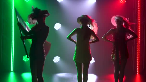 Theateraufführung von drei schönen Tänzerinnen. Silhouetten junger Frauen posieren in Anzügen in den Farben der italienischen Flagge vor dem Hintergrund heller Scheinwerfer. Nahaufnahme. — Stockvideo
