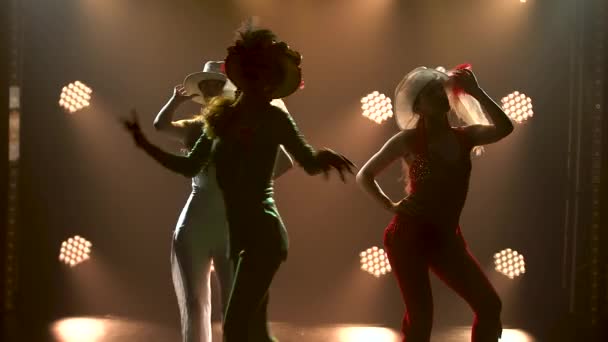 Yeşil, beyaz, kırmızı, parlak, ince takım elbiseler ve orijinal şapkalarla dans eden üç güzel genç kadının silueti. Tiyatro kadın dans gösterisi. Kapat.. — Stok video