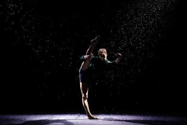 Portret van een mannelijke danser in een acrobatische pose op een zwarte achtergrond met vallende sneeuw. — Stockfoto