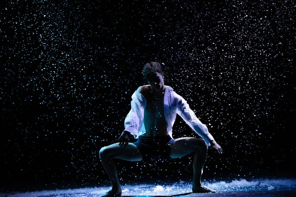 年轻英俊的男子在降雪的背景下跳舞.在演播室光的光芒中，舞者的轮廓。靠近点. — 图库照片