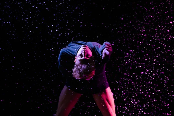 在降雪和工作室灯光的背景下，一个男芭蕾舞蹈演员在黑暗的演播室里表演的肖像。靠近点. — 图库照片