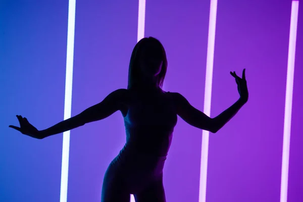 霓虹灯中紫色工作室背景的迷人模型的轮廓。漂亮的女人穿着内衣摆姿势,双手摆出性感的姿势.靠近点. — 图库照片