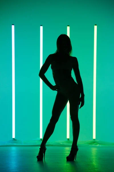 Sexy fitness body woman stands posing against the backdrop of neon lamps and green backlight. Silhouette of perfect body. Close up. — Stock Photo, Image