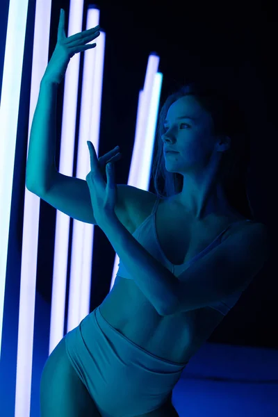 Attraktiv brunett modell på blå studio bakgrund i neonljus. Vackra kvinnor i underkläder poserar med händerna i en sensuell pose. Närbild. — Stockfoto
