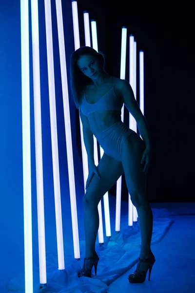 Ritratto bella donna bruna calda in lingerie in posa in uno studio fotografico su uno sfondo scuro con lampade al neon luci blu. Da vicino.. — Foto Stock