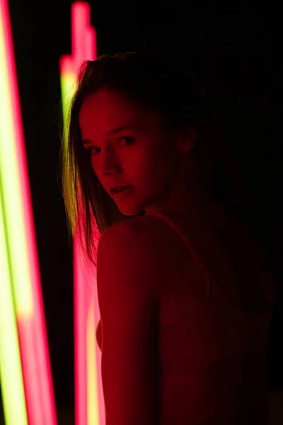 Sexy young woman with sensual lips posing in a photo studio on a dark background with neon lamps lights. Close up. — Stock Photo, Image