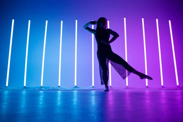 Sexig söt ung kvinna dansare dansar och poserar i ett rum med ljusa neon blå lila färg. Silhuett av en sportflicka njuter av en dans i studion med neonljus. — Stockfoto