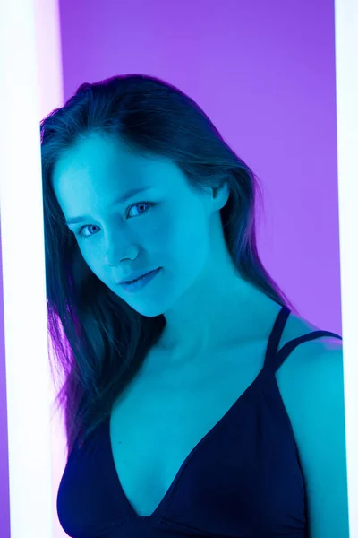 カメラに情熱的に見て魅力的な天然の若い女性の肖像画。このモデルは、明るいネオンランプを背景に青い光の光の中でポーズをとっています。閉じろ!. — ストック写真