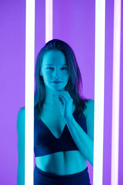 Fashion art portrait of young and sexy female model posing in blue lights against the backdrop of bright neon lamps. Close up. — Stock Photo, Image