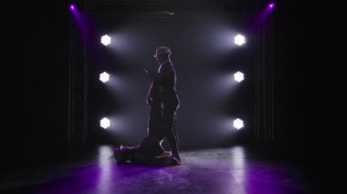 Denge pozisyonunda iki erkek akrobat. Takım çalışmasında karmaşık numaralar yapan güçlü atletik adamların siluetleri. Siyah bir arka planda sahne ışıkları altında. Yavaş çekim.