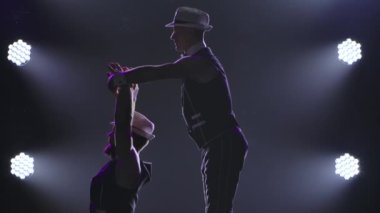 İki erkek jimnastikçi bilanço üzerinde akrobatik numaralar yapıyor. Siyah arka planda spot ışıkları olan iki adamın siluetleri. Ağır çekimde kapat..