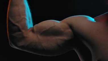 Profesyonel vücut geliştirme sporcusu güçlü kaslarını göstererek kolundaki pazıları esnetir. Spor ve vücut kavramı. Resim stüdyoda siyah bir arkaplanda çekildi. Ağır çekim. Kapat..