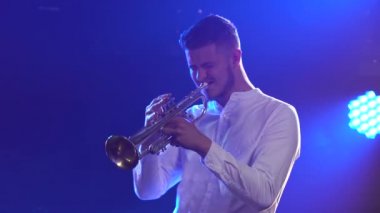 Trompet çalan bir erkek müzisyenin solo konseri. Yetenekli bir adam, mavi ışıklı karanlık bir stüdyoda klasik enstrümantal müzik melodisi çalar. Yan görüş. Kapat..