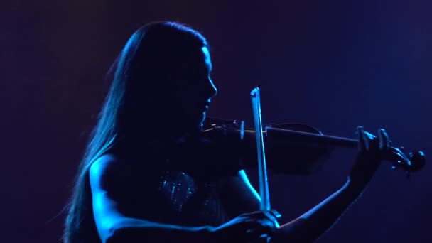 Sylwetka pięknej brunetki muzyk kobieta w błyszczącej sukience gra na skrzypcach w ciemnym studio z niebieskim oświetleniem. Zamknij się.. — Wideo stockowe