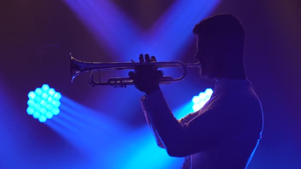 Solo concert van een mannelijke muzikant die trompet speelt. Een getalenteerde man voert een melodie van klassieke instrumentale muziek uit in een donkere studio met blauw licht. Zijaanzicht. Sluiten.. — Stockvideo