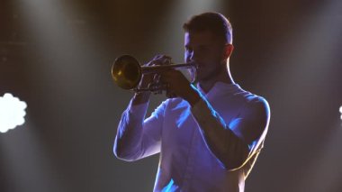 Genç bir adam, karanlık bir stüdyoda sahne ışıklarıyla dramatik duygular içeren bir melodi çalıyor. Kapat..