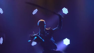 Mor ışıklarla dolu karanlık bir stüdyoda kılıçlarla dövüşen iki şövalyenin tiyatro gösterisi. Tarihsel zırhlı adamların siluetleri. Kapat..