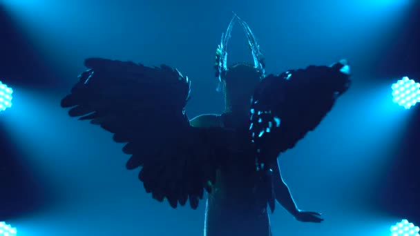Silhuett av en dansande kvinna i en kort klänning och med vingar på ryggen. Grekiska gudinnan Artemis i en teatralisk sångshow med blått neonljus. Närbild. — Stockvideo